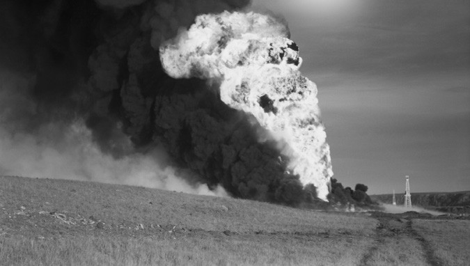 Figure 14-1 “Flare at Turner Valley oil field, Alberta.” Black and white photograph of the flaring of natural gas from a well in Turner Valley. A vast column of black smoke and fire bursts hundreds of feet into an open field and the open sky from an oil rig in Turner Valley. The fire appears fierce and out of control, with dense, dark smoke rising vertically alongside the flames. In the corner of the picture is an oil rig that is dwarfed by the tower of flame and smoke.