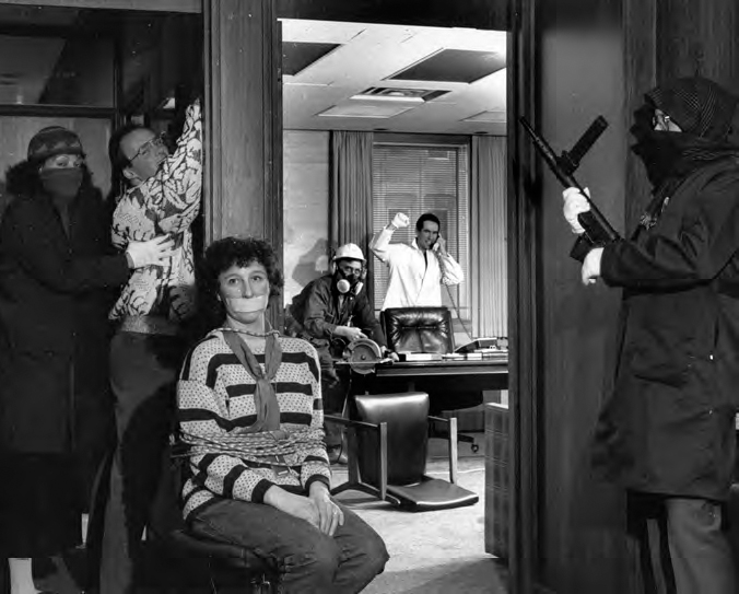 A photograph shows the interior view of a house with some people having guns in their hands and some hostages.
