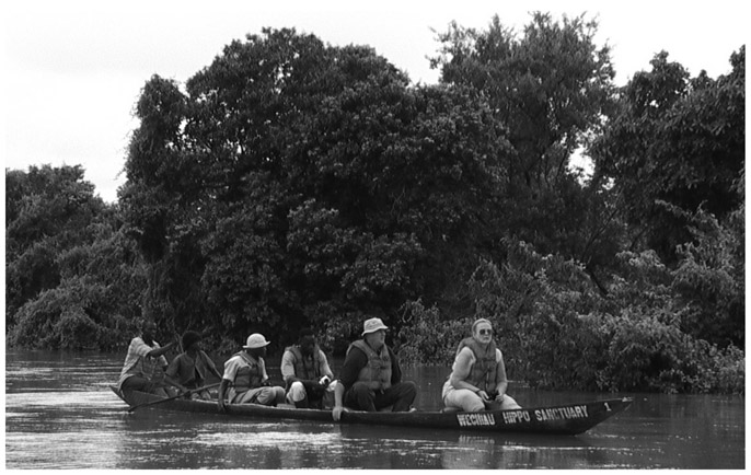 A black and white photograph of six people paddling on a Black Volta boat looking for the hippos on the river.