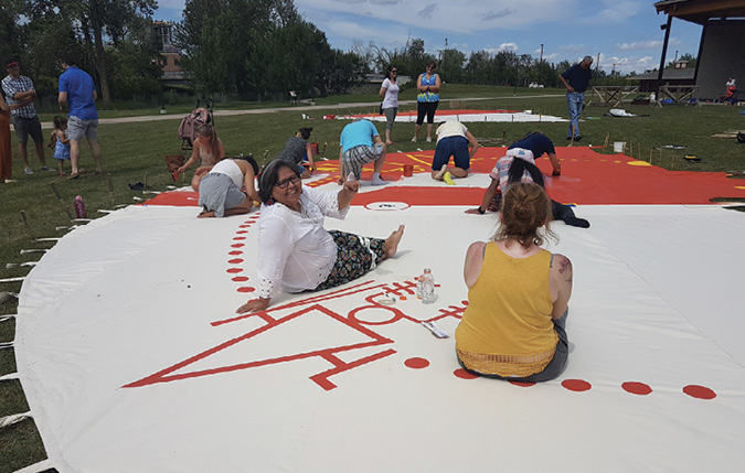 Colour Photograph: People painting the ii’ taa’poh’to’p  tipi canvas at Stampede Park Indigenous Peoples Village. 