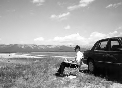A photograph shows a piece of land and a man sitting on a chair beside a car. Mountain and clouds can also be seen.