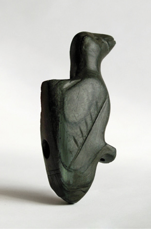 Colour photograph. Photo of a black stone carving of a bird. The bird is facing away, and its body is the main part of the carving. A circular hole is visible in the body.
