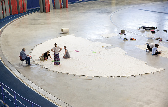 Colour Photograph: Birds eye view of people helping sketch out the ii’ taa’poh’to’p tipi design on large canvas.