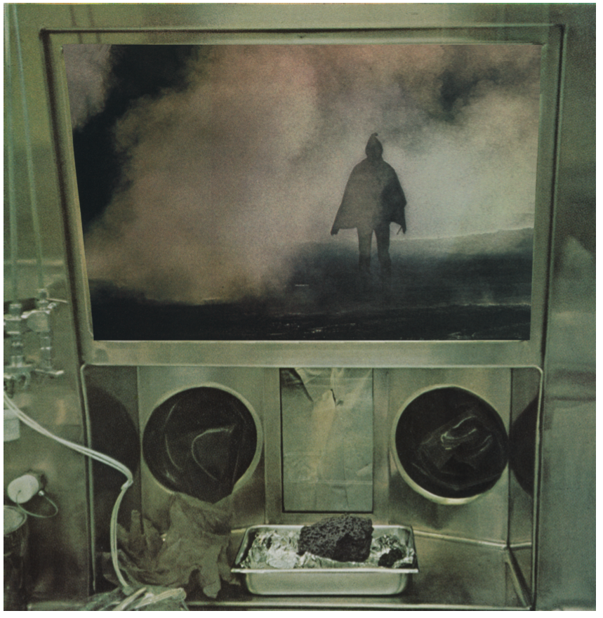Colour photo collage: The interior of a metal fume hood, with gloves and a tray containing a substance; through a window is seen a figure in a cape and hood, surrounded by mist.