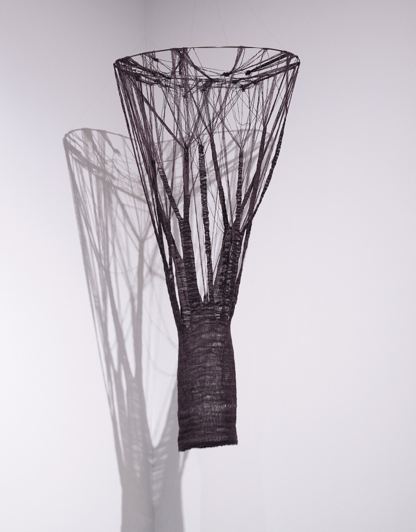 Photo: a brown hanging, almost shaped like a basketball net, with disparate strings that resolve themselves into a tube. The shadows from the art are dramatic. 