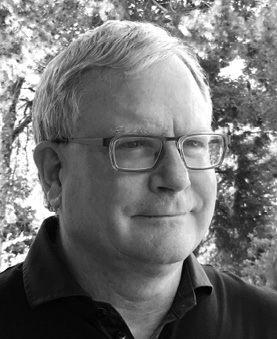 Black and white photograph: Portrait of a middle-aged man with short hair and glasses. He is looking slightly to the side.