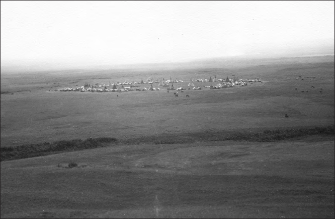 A photograph shows an ariel view of large land. Several tents can be seen on the land.