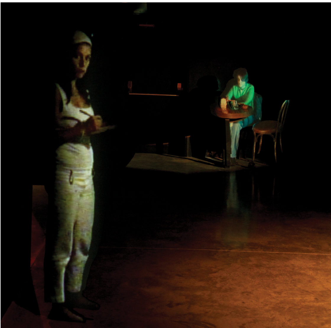 Colour photograph: An installation with projections, showing a waitress standing in the foreground with an order pad, and a man seated at a café table in the background.