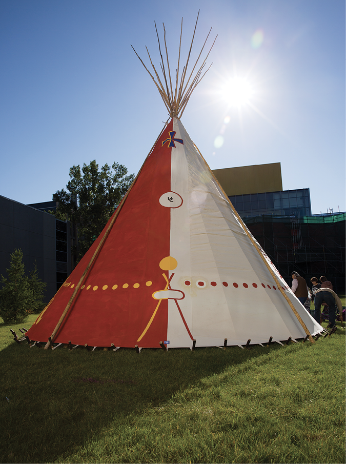 Colour Photograph: Backside view of ii’ taa’poh’to’p painted tipi, with symbols on red and white painted canvas.