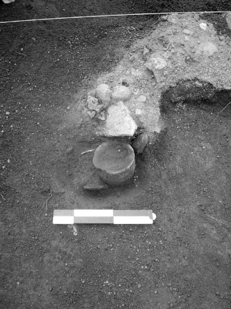 A pot lies adjacent to large broken pieces of a stone.
