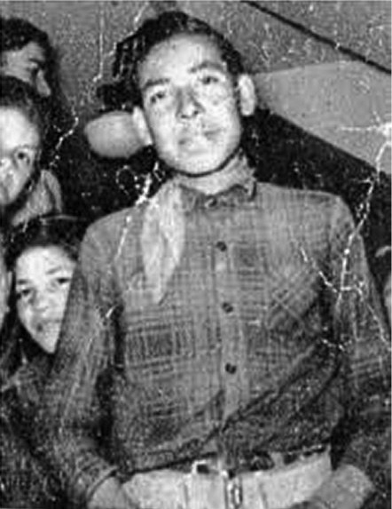 Black and white photograph: Teenage Indigenous boy from the waist up wearing a western-style shirt and scarf.