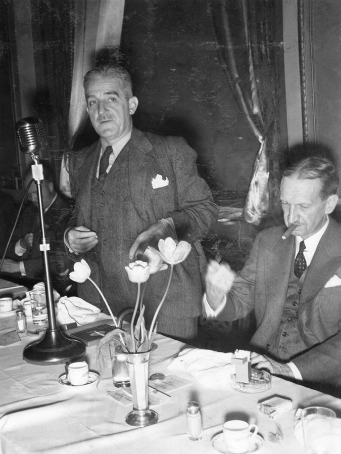 Stratford was the leading figure in developing Imperial Oil’s research operations between the 1920s and 1940s. In this photo he is shown with R.V. LeSueur, president of International Petroleum and later Imperial Oil after G.H. Smith. It appears to be a formal dinner. Both men have moustaches and are in three piece suits at a set table. Stratford is standing and speaking, while LeSueur is smoking a cigar and staring at his fist.