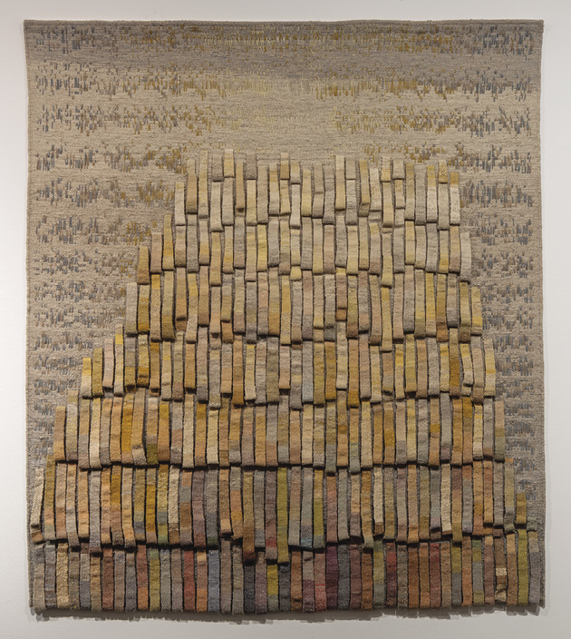 Photo: large tan, blue, grey, and brown artwork. There are patches of colour along the top and down the sides that blend into material handles formed into seven rows that get darker and darker.