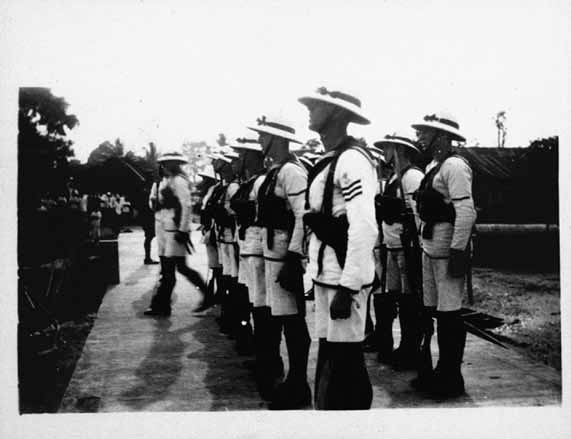 A black and white photograph shows officers in uniform standing in two rows. One of the officers is stepping forward from the front row.