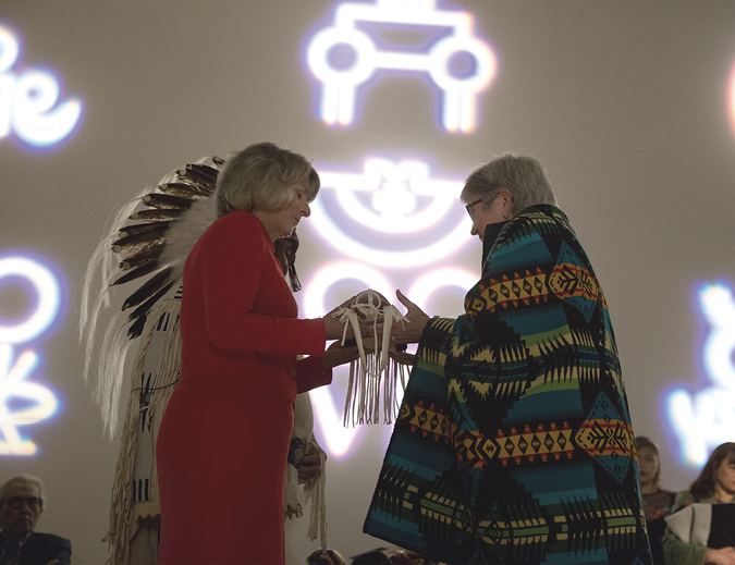 Colour Photograph: Presentation of the completed Strategy from the Provost to the President, with ii’taa’poh’to’p symbols in the background. 
