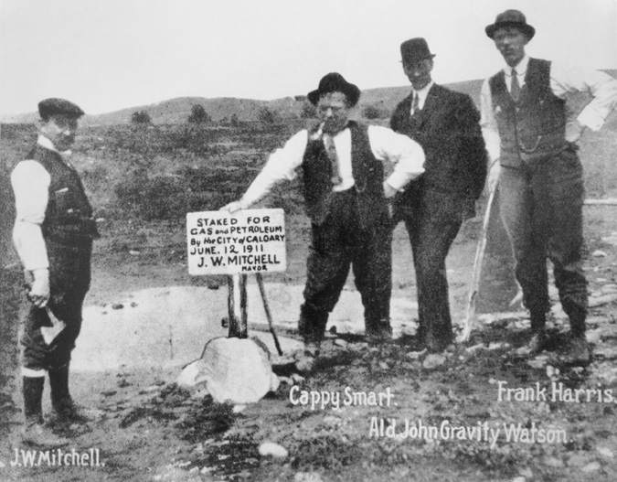Figure 1-2 “Gas and petroleum claim being staked by the City of Calgary” Black and white picture of four men dressed in business clothes standing in a muddy field. From left to right, the men are identified by writing underneath their picture. Calgary mayor John W. Mitchell stands to the left of the three other men in his shirt sleeves and a vest and is holding a hatchet in his right hand. “Cappy” Smart, also in shirt sleeves and with an open vest, leans on a sign that reads “Staked for Gas and Petroleum By the City of Calgary June 12, 1911. J.W. Mitchell, Mayor.” Alderman John “Gravity” Watson stands with his hands behind his back while Frank Harris leans on what appears to be a walking stick.
