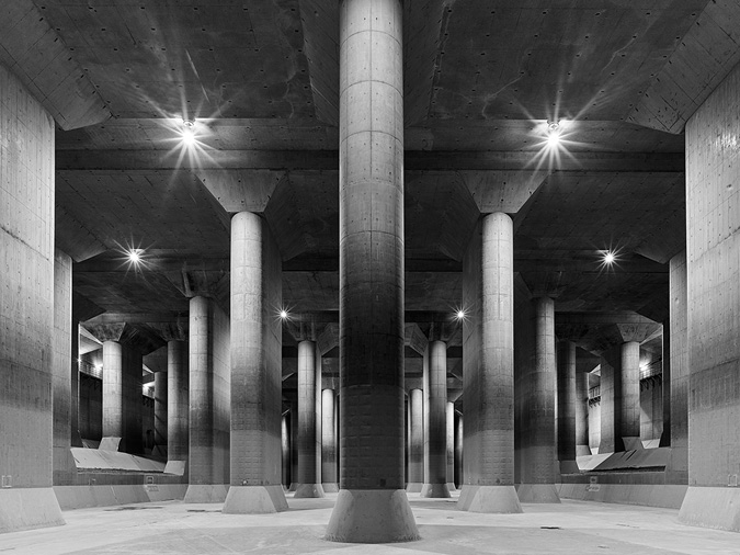 Dozens of massive concrete pillars in a massive empty concrete water chamber building are lined up, orderly, clean and the space is open and light.