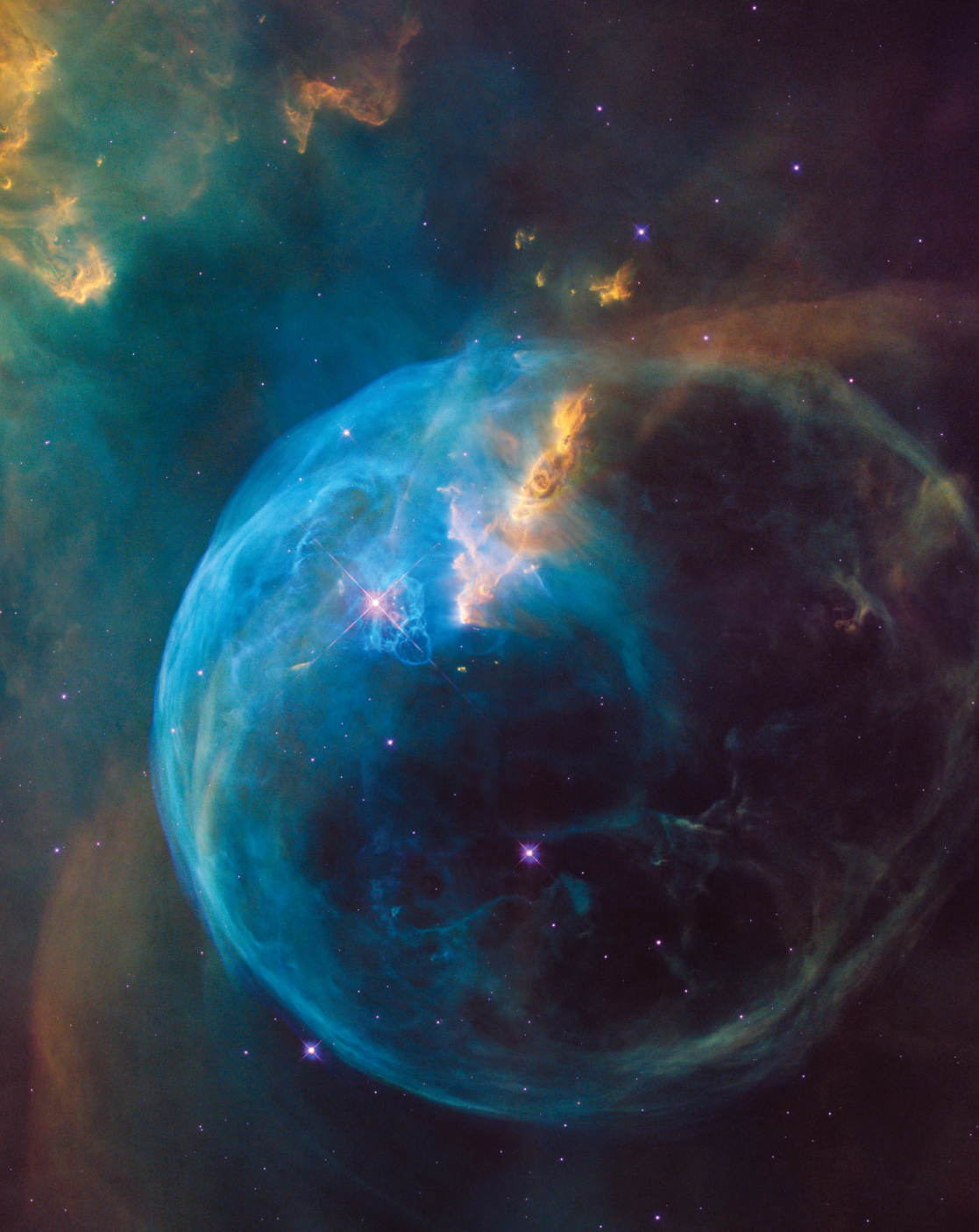 A picture of space depicts a wispy blue nebula in the shape of a circle studded with purple stars. Gold coloured wisps also swirl inside the nebula, and descend from the top left of the image.