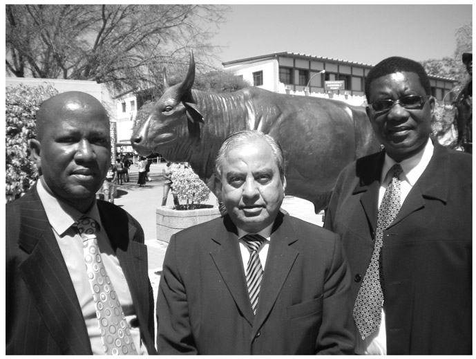A black and white photograph of Professor Keshav C. Sharma, Professor Mpho Molomo, and Dr. Mogopodi H. Lekorwe, standing in front of the sculpture of an ox.