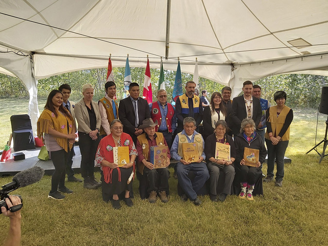 A group of signatories on the Peel Land-Use Plan for the Peel Watershed are posing for a group photo to sign off, together, on the plan. Seated are five elders holding the printed plan, with other stakeholders standing behind the elders.