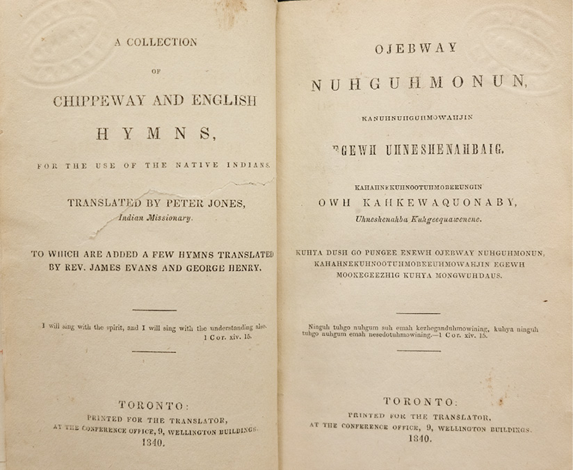 Colour photograph. A yellowed open book, with a two-page spread. The sides are matching title pages, with the left written in English, and the right in Anishinaabemowin. 