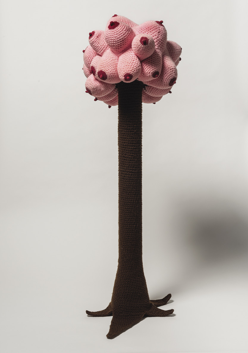 Photo: a brown knit tree trunk with a profusion of knit boobs on top — pink blobs with red nipples.