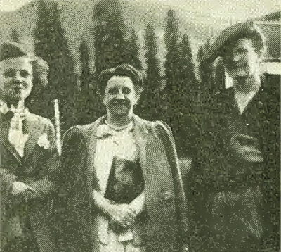 Photo : cliché sépia flou de trois femmes devant des sapins et une montagne. Elles portent des vêtements des années 1940 et sourient devant l’appareil photographique. 