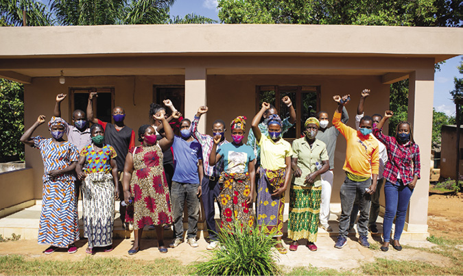 Colour photograph: A group of women and men wearing Covid masks stand with fists raised in front of the portico of a building
