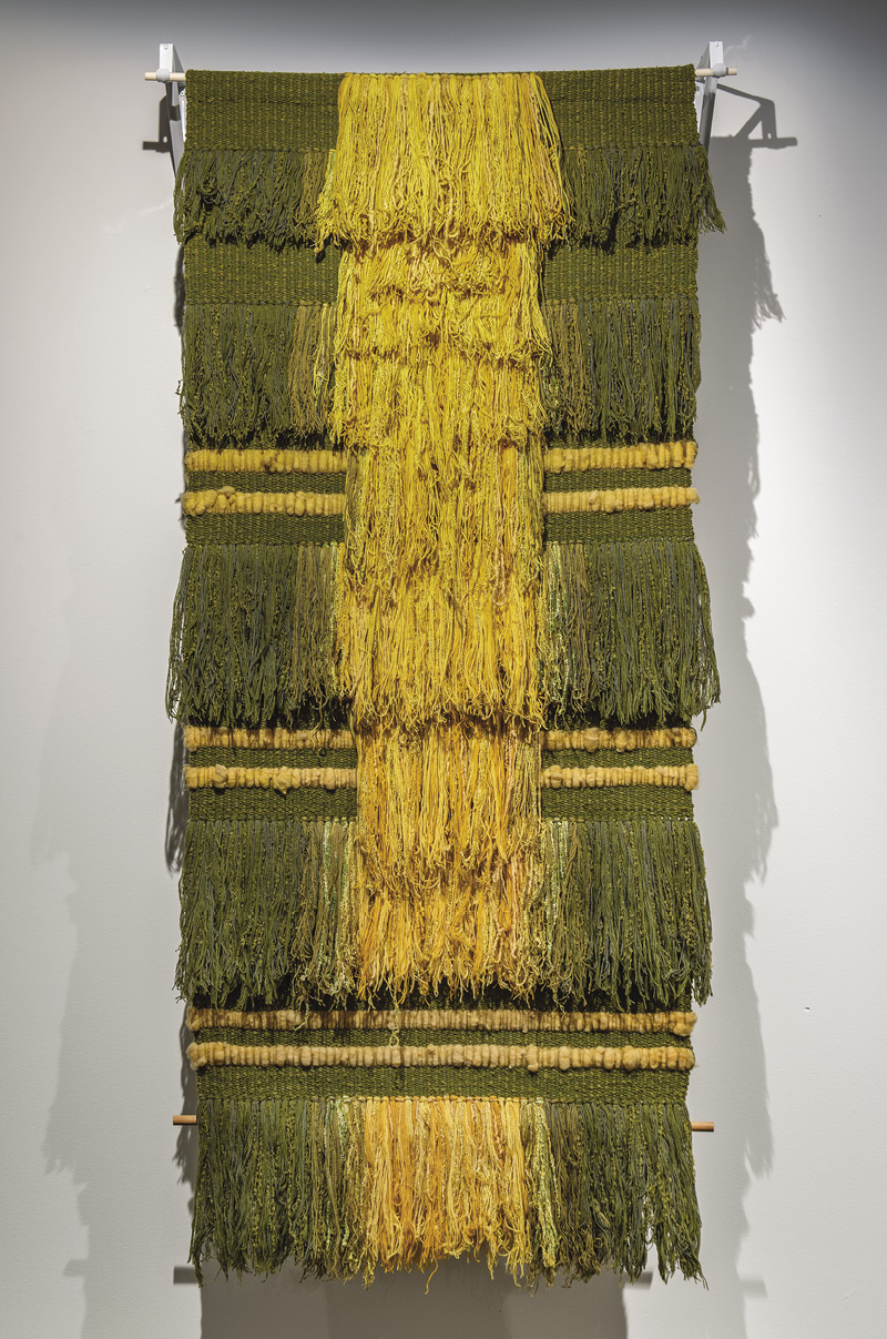 Photo : Pièce murale vert olive et jaune moutarde. Elle est composée de cinq rangées et de cinq franges, et est principalement verte avec une large bande jaune au milieu. 