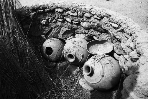 Three large pots placed inside a hole in the ground. The pots decrease in size from right to left. An old dish and some hay are placed beside them.