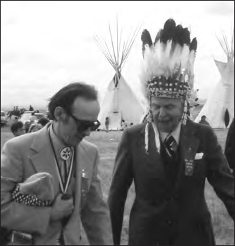 A photograph shows two men in formal dress, one of them has a crown on his head. Two tents with spikes on the roof can be seen in the background.