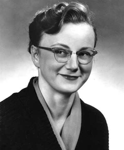 Black and white photograph. Head and shoulders portrait of a young woman. She is wearing horned-rimmed glasses, lipstick, and a black and cream cardigan.