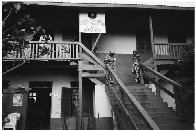 A black and white photograph of Manya Krobo Queenmothers Association Resource Centre. It is a two storey building, with few women standing on the stairs and near the railings.