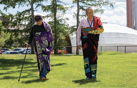 Colour Photograph: Traditional knowledge keepers, Andy Blackwater (left) and Calvin Williams (right), walking across the grass.