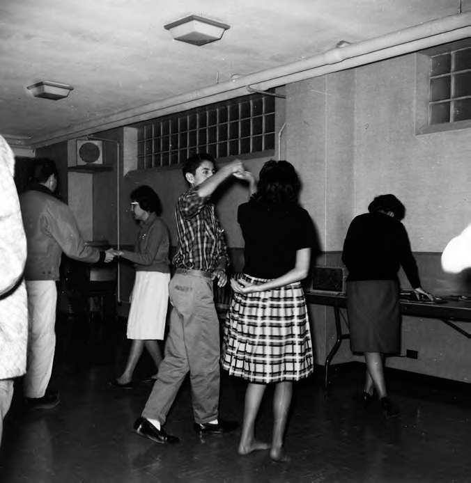 A photograph shows several people dancing in pairs wearing casual dresses. A window and ceiling lights can be seen.
