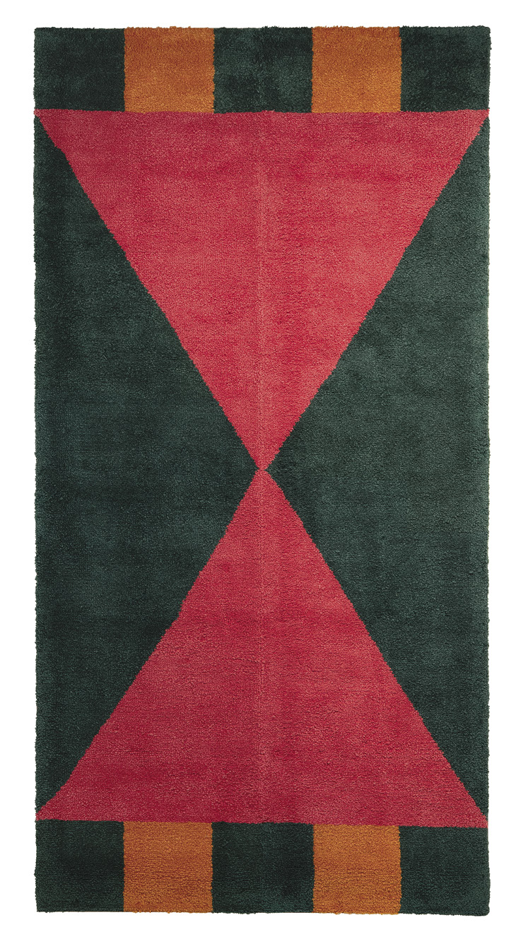 Photo: vertical green rug with two large red triangles whose points meet in the middle. Two orange square anchor the triangle at the top and the bottom to the edges. 