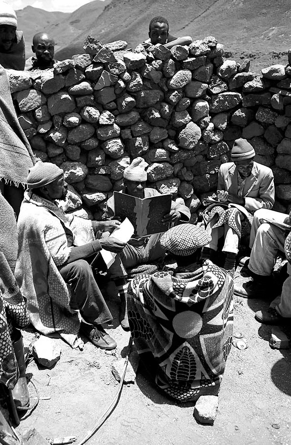A black and white photograph of people sitting in front of a pile of stones and reading books.
