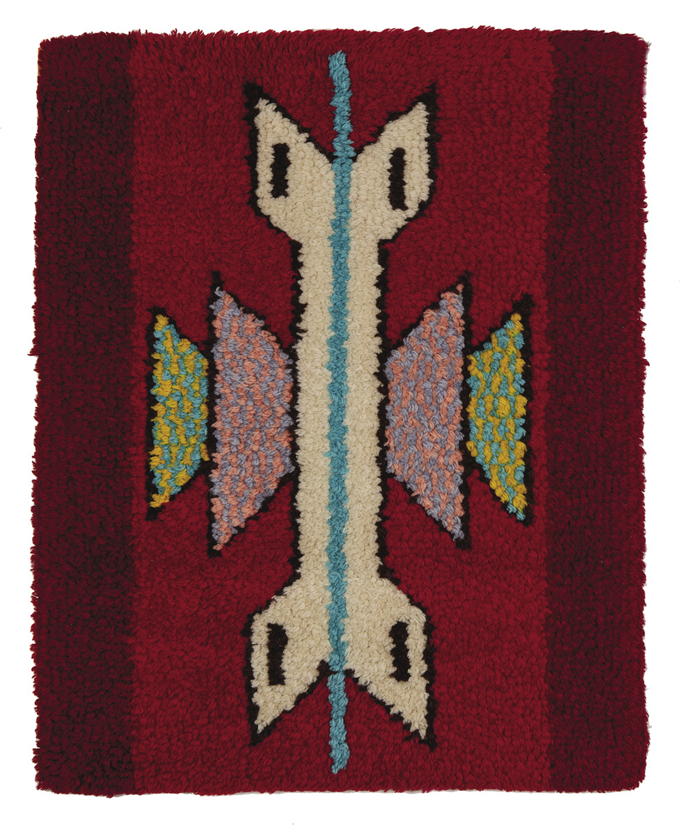 Photo: red rug, rectangle, in portrait orientation. Dark red stripes along the right and left edge, and an arrow shape that has no point running vertically. It is white, outlined in black, with a turquoise strip running through it. There are shapes coming out the middle on both sides filled with yellow and turquoise, pink and purple. 