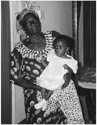 A black and white photograph of Manya Krobo woman cradling her foster child, inside a room.