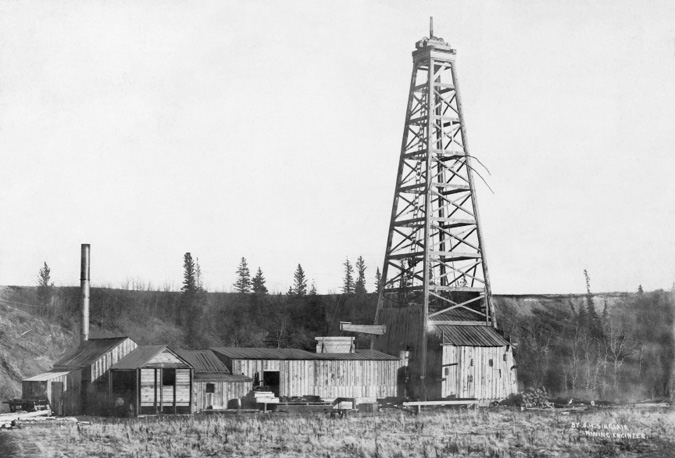 Figure 1-5. “Calgary Petroleum Products #1 Well” Back and white photograph of the Dingman #1 oil derrick and several wooden outbuildings off the rig at Calgary Petroleum Products’s No. 1 wellsite in Turner Valley. Those building house pump, boiler, steam engine, and probably a workshop necessary to keep the rig running. There are some pine trees in the background, framing the wellsite.