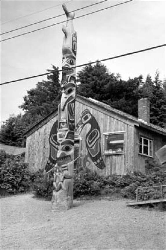 A long totem pole exquisitely carved with many figures and erected in a yard of a small house.