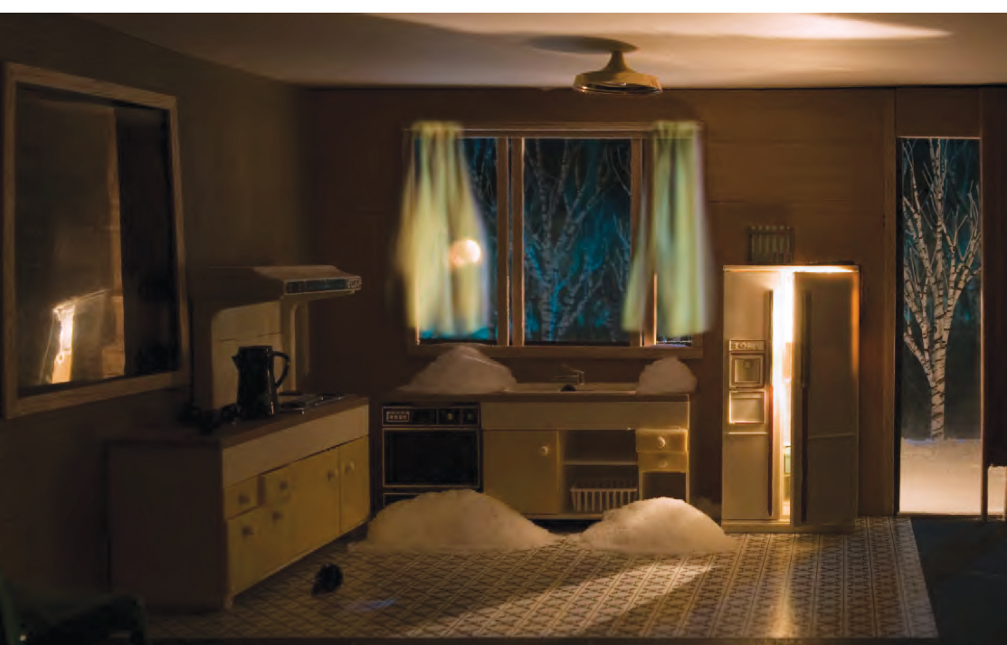 Colour photograph: A diorama of a kitchen, with mounds of snow on the floor and the counter; the fridge door is open and light is coming out.  Through an open patio door we see snow and a birch tree.