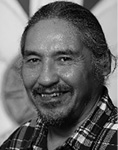 Black and white photograph: Portrait of a man with a beard smiling and wearing a plaid shirt.