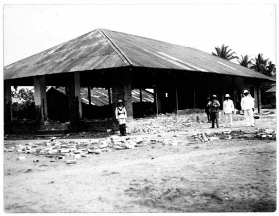 A black and white photograph shows a few officers in different uniforms standing in front of a destroyed courthouse.
