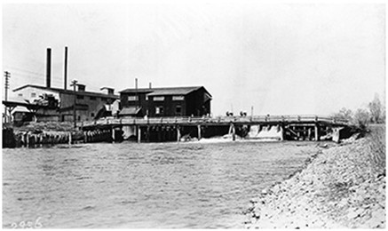 A bridge constructed over a river connects to the Calgary Water Power Company hydroelectric plant.