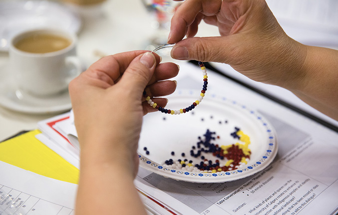 Colour Photograph: A person’s hands working on beading a bracelet.