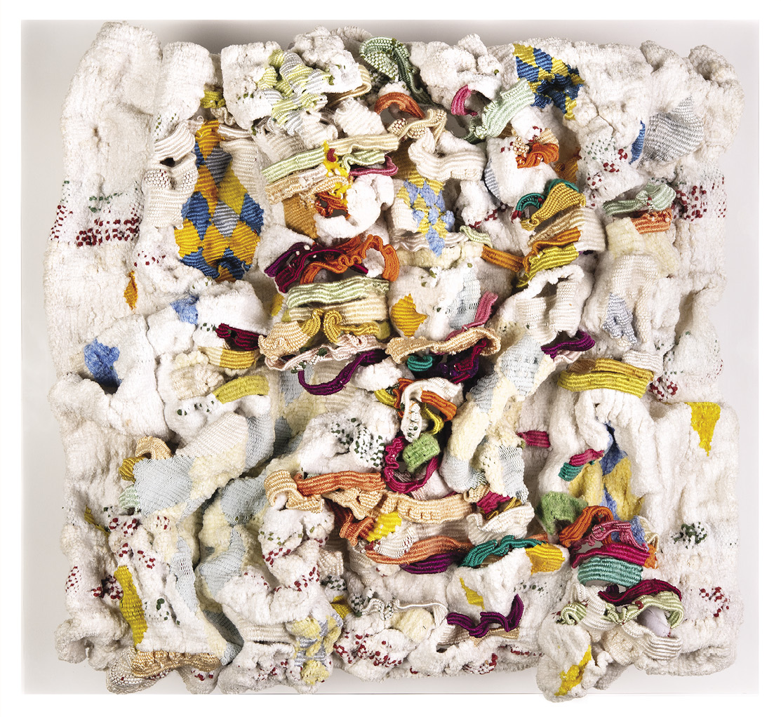 Photo: a jumble of mostly white textiles with pops of yellow, orange, green, blue, and purple in a square, 3d form.