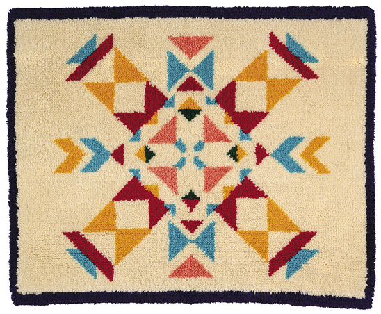 Off-white rug outlined in black with a turquoise, red, and orange geometric pattern pointing into the middle. 