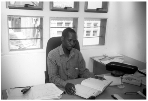 A black and white photograph of inkosi Mlaba, sitting at his desk in his office, doing paperwork.