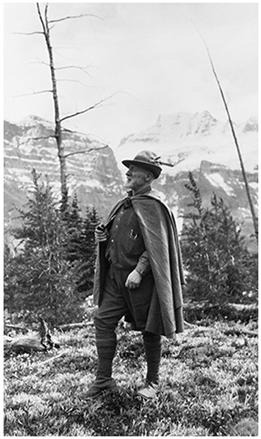 A. O. Wheeler stands on some grass. A snow capped mountain is in the background.